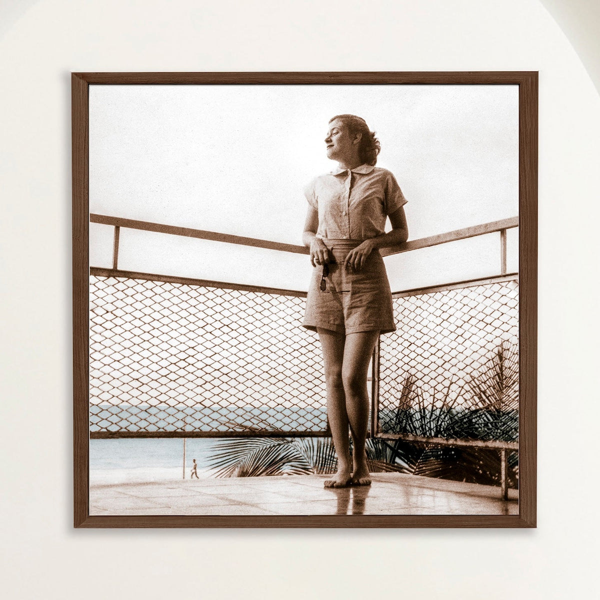 Sepia photograph with colour touches of a 1950s woman on a balcony above Playa Cojimar, framed in oak. Close view.