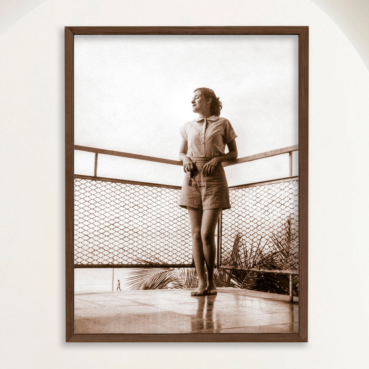 Sepia photograph of a 1950s woman on a balcony above Playa Cojimar in vertical format, framed in oak. Close view.