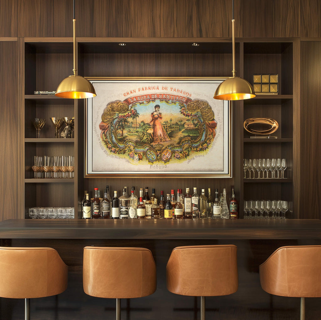 A framed artwork of a vintage Cuban cigar label art hangs on a dark wood bar wall in an elegant restaurant or hotel. Art work features a 1890s colorful design and gold coin awards.
